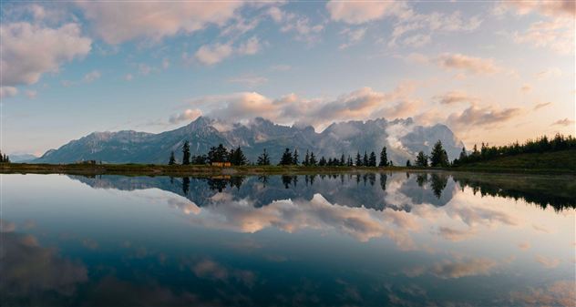 Eine beeindruckende Landschaft mit hohen Bergen und sanften Wolken. Ein ruhiger See spiegelt die Berge und den Himmel wider.