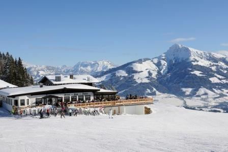 Ein gemütliches Restaurant in den Bergen, umgeben von schneebedeckten Gipfeln. Skifahrer und Besucher genießen die Aussicht auf die malerische Winterlandschaft.