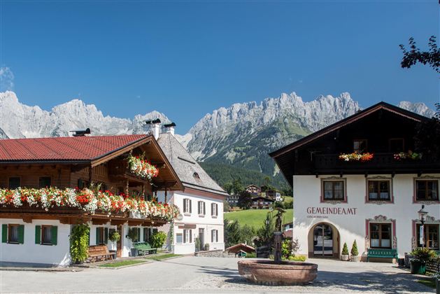 A picturesque alpine landscape with traditional wooden houses. In the background, majestic mountains rise under a clear blue sky.