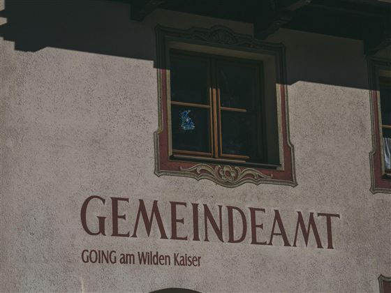 The image shows the facade of a building with the inscription "Municipality" and "Going am Wilden Kaiser." A window is visible, and the walls are simply designed.