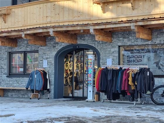 A sporting goods store with an inviting entrance. Various clothing items hang on racks in front of the store.