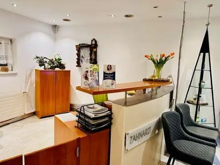 A friendly reception area in a dental practice. There is a wooden counter, chairs, and decorative plants.