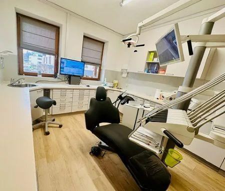 A modern dental office room with a treatment chair and a screen. The walls are bright, and there is plenty of space for medical equipment.
