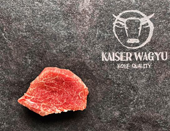 Ein rohes Stück Wagyu-Fleisch auf einer dunklen Oberfläche. Daneben steht das Logo "Kaiser Wagyu" für höchste Qualität.