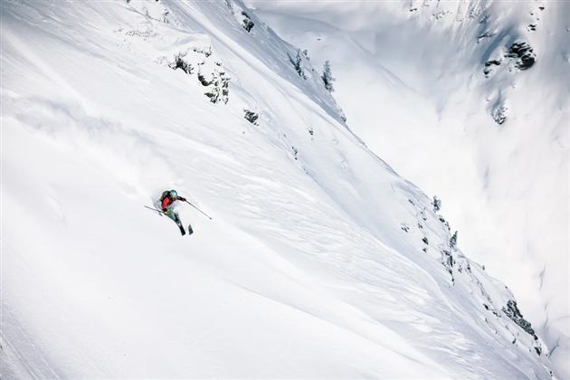 Ein Skifahrer fährt über eine schneebedeckte Piste in den Bergen. Die Landschaft ist beeindruckend und die Umgebung wirkt unberührt.