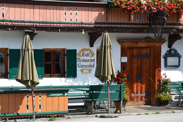 A traditional restaurant with an inviting entrance door and blooming plants. The green shutters and sun umbrellas give the place a cozy charm.
