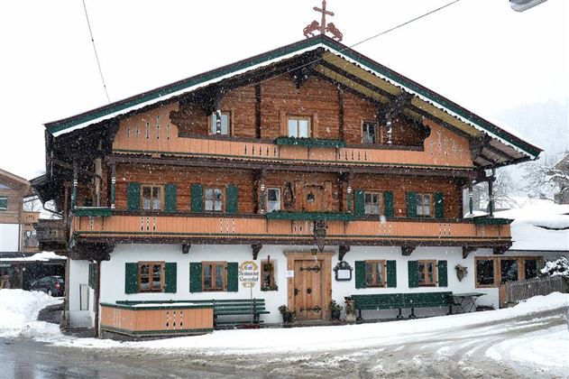 Een traditioneel houten huis in Beierse stijl, omringd door sneeuw. De groene luiken en balkons geven het gebouw een charmante uitstraling.