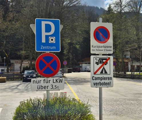 Ein Parkbereich mit verschiedenen Verkehrsschildern. Es gibt Hinweise zu Parkregeln und einem Campingverbot.