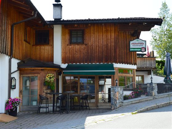 A cozy inn with a wooden facade and a terrace. Surrounded by flowers and an inviting ambiance.