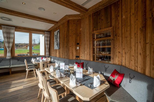 Een gezellig restaurant met houten wanden en een groot raam. De tafels zijn feestelijk gedekt en er zijn comfortabele zitgelegenheden.