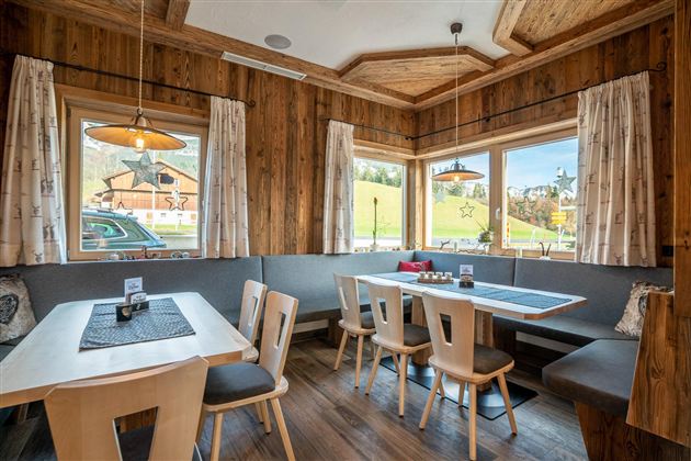 Een gezellige eetkamer met houten wanden en grote ramen. Er zijn tafels met houten stoelen en een uitnodigende sfeer.