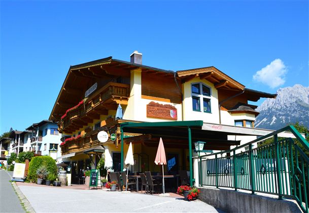A charming building in alpine style with balconies and colorful flowers. The surroundings are clean and friendly, with a view of the mountains.