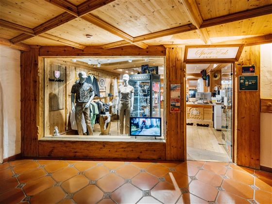 Een winkel met houten bekleding en een etalage, waarin kleding op manieken wordt gepresenteerd. Op de achtergrond zijn andere producten en een receptiebalie te zien.