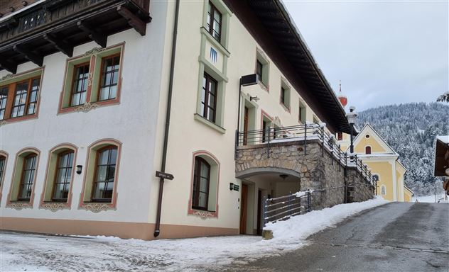 Een schilderachtig gebouw in de bergen, omgeven door sneeuw. De architectuur is traditioneel met houten versieringen en grote ramen.