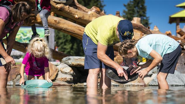 A group of children and adults discovers fossils or gemstones in a shallow body of water. They collect and examine the finds with bowls and sieves.