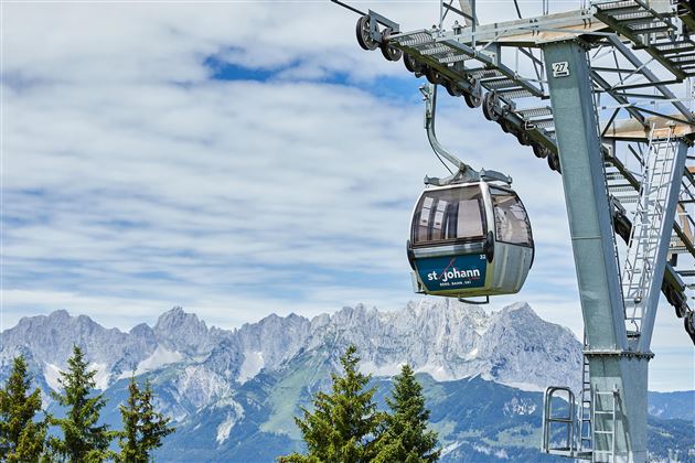 Een kabelbaan zweeft boven een indrukwekkend berglandschap. De lucht is bewolkt, en de bergen op de achtergrond zijn majestueus.