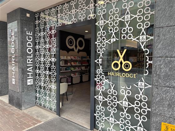 A hair salon with the sign "HAIRLODGE" and a modern entrance. The windows are decorated with stylish patterns and scissor symbols.