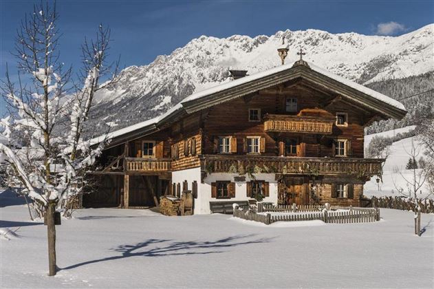 Een traditioneel houten huis in de sneeuw, omgeven door bergen. Het idyllische winterlandschap straalt rust en gezelligheid uit.