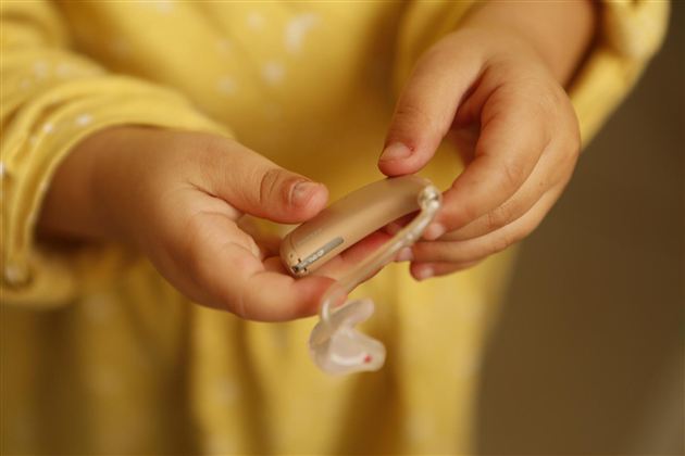 A child is holding a hearing aid in their hand. The hands are small and appear delicate.