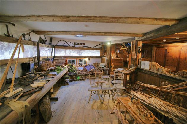 Ein traditioneller Werkraum mit Holzwerkzeugen und handgefertigten Gegenständen. Der Raum ist rustikal gestaltet und strahlt eine gemütliche Atmosphäre aus.