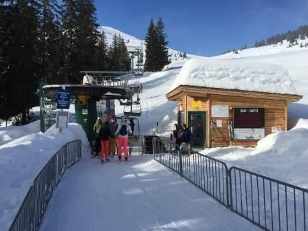 A ski lift station in a snow-covered area.  
People are standing in line to get on the lift.