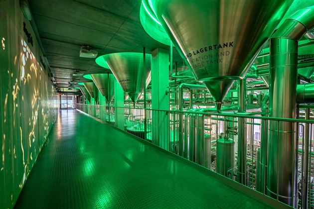 Een moderne binnenruimte met grote, groene opslagtanks en metalen leidingen. De vloer is groen en de ruimte heeft een industriële sfeer.