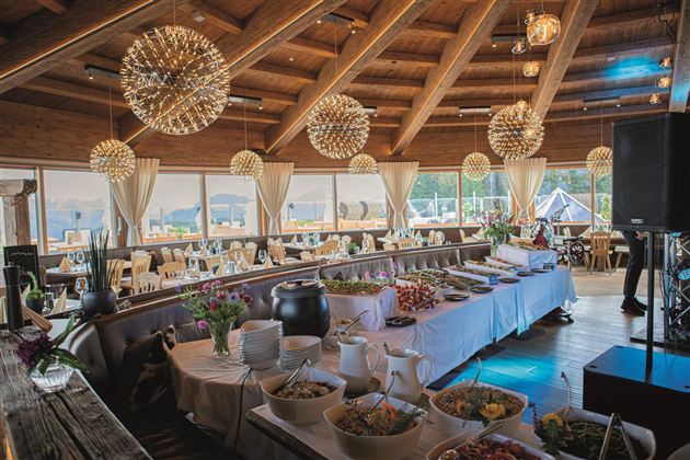 Ein stilvolles Restaurant mit Holzbalkendecke und großen Fenstern. Der Tisch ist reichlich mit verschiedenen Speisen und Dekorationen gedeckt.