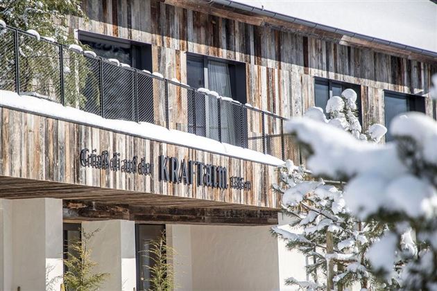 Een houten gebouw met moderne architectuur in de sneeuw. De tekst "KRAFTHAUS" is duidelijk zichtbaar.