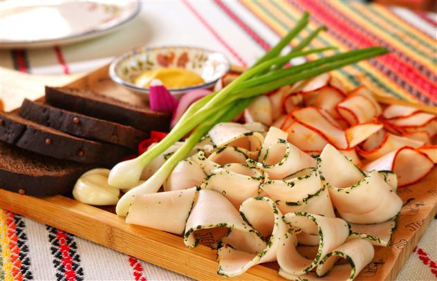 Een selectie van kaas, ham en vers brood ligt op een houten schaal. Op de achtergrond zijn meer voedingsmiddelen en een glas melk te zien.