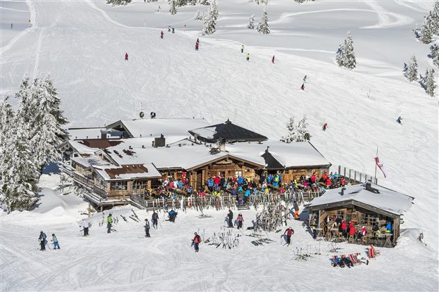 Een gezellige skihut omringd door sneeuw en bergen. Veel mensen genieten van het winterlandschap en het skiën.
