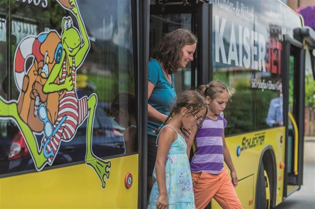 A woman and two girls are getting out of a colorful bus. The bus has a striking design featuring a drawing of a frog character.