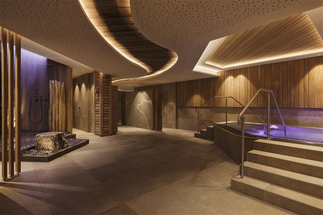 An elegant spa area with wooden paneling and soft lighting. A staircase leads to a water area with a relaxing atmosphere.