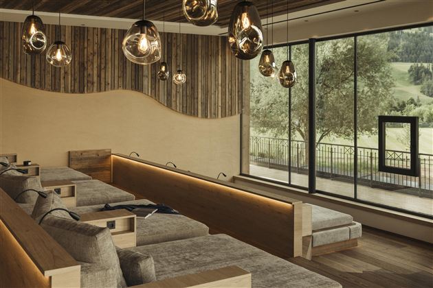 A modern, cozy living room with wood paneling and stylish lamps. Large windows offer a view of the greenery.