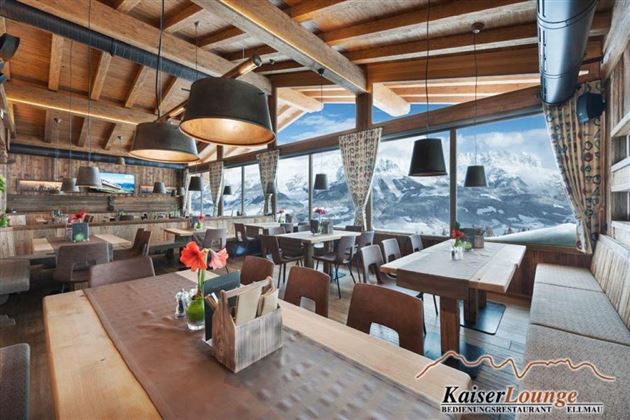 Ein gemütliches Restaurant mit Holzdekor und modernen Lampen. Große Fenster bieten einen Blick auf die Berge und lassen viel Tageslicht herein.