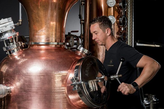 Ein Mann arbeitet an einer großen Kupfer-Destille. Im Hintergrund sind verschiedene Messgeräte sichtbar.