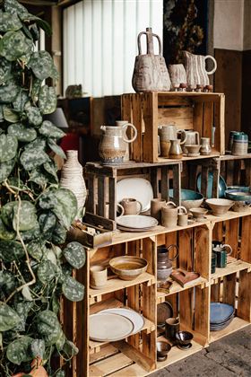 Eine stilvolle Regalwand aus Holzkisten mit verschiedenen Töpfen und Geschirr. Im Hintergrund sind grüne Pflanzen sichtbar, die eine gemütliche Atmosphäre schaffen.