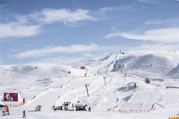 Eine verschneite Landschaft mit Skiliften und Pisten. Der Himmel ist klar und blau, ideal für einen Skitag.