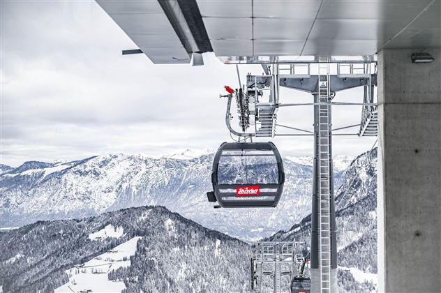 A cable car in the mountains on a snowy day. In the background, snow-covered mountains and a clear sky can be seen.