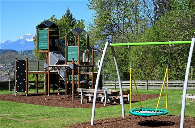 A playground with a slide and swings. In the background, there are green trees and mountains.