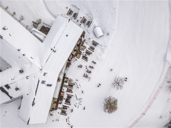 Een met sneeuw bedekt gebied met een groot gebouw en meerdere kleine hutten. Op de achtergrond zijn besneeuwde landschappen te zien.