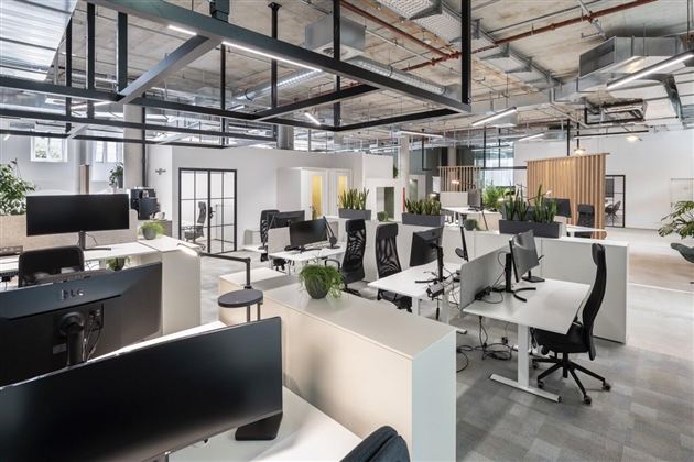 Moderner Großraumbüro-Arbeitsplatz mit weißen Schreibtischen, schwarzen Monitoren und offener Deckeninstallation.