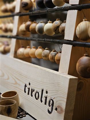 A rustic sales stand with handcrafted wooden ornaments and mugs. The inscription "tirolig" on the wooden board emphasizes the origin of the products.