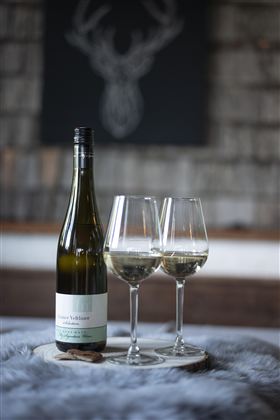 Een fles witte wijn staat naast twee glazen op een houten plank. Op de achtergrond is een stijlvolle decor te zien.