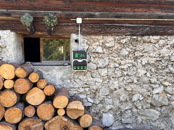 A stack of wood lies against a stone wall. Above the window hangs a sign with a bicycle symbol.