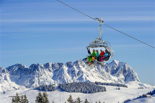 Een groep skiërs rijdt in een gondel over besneeuwde bergen. De heldere lucht en het indrukwekkende landschap creëren een winters sfeer.