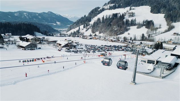 Zasněžená krajina s lyžařskými vleky a lyžařskou oblastí. V pozadí jsou hory a typické alpské chaty.