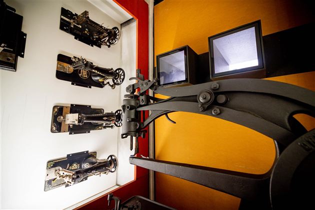 Eine alte Druckmaschine steht im Vordergrund. Im Hintergrund sind historische Druckwerkzeuge an einer Wand ausgestellt.