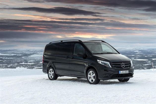 Ein schwarzer Mercedes-Van steht auf schneebedecktem Boden. Im Hintergrund ist eine weite, winterliche Landschaft mit einem farbenfrohen Himmel zu sehen.