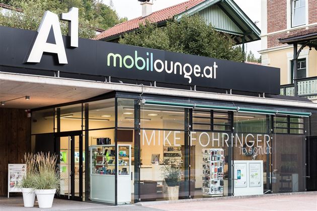 Ein modernes Geschäft mit dem Logo "mobilounge.at" und großen Glasfenstern. Neben der Eingangstür sind verschiedene Produkte und Dienstleistungen ausgestellt.