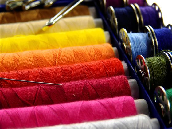 A collection of colorful sewing threads in various colors. Sewing needles are also visible and complement the image.